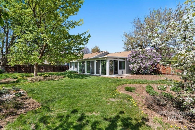 rear view of property with a fenced backyard, a yard, and a sunroom