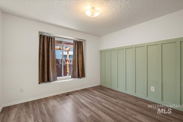 empty room with visible vents, a textured ceiling, and wood finished floors
