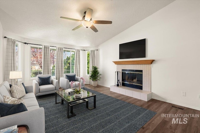 living area with a ceiling fan, a textured ceiling, visible vents, a fireplace, and wood finished floors