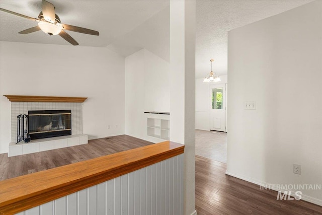 unfurnished living room with a fireplace, vaulted ceiling, wood finished floors, baseboards, and ceiling fan with notable chandelier