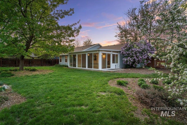 back of house at dusk featuring a sunroom, a lawn, and fence