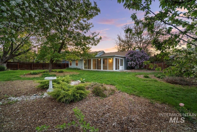 rear view of house featuring a sunroom, fence, and a yard