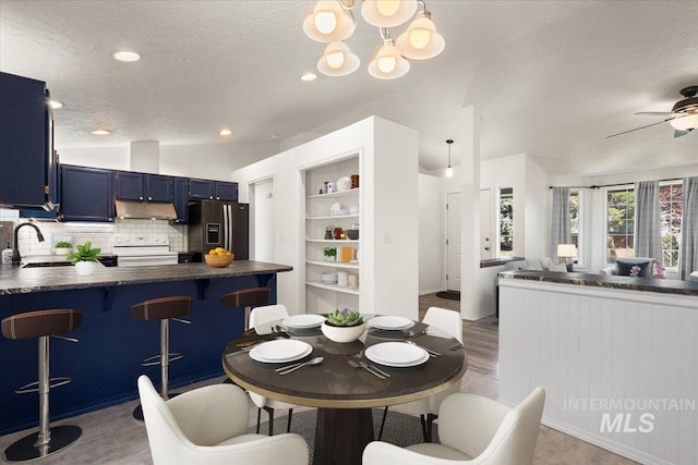 dining space featuring a ceiling fan, vaulted ceiling, a textured ceiling, and wood finished floors