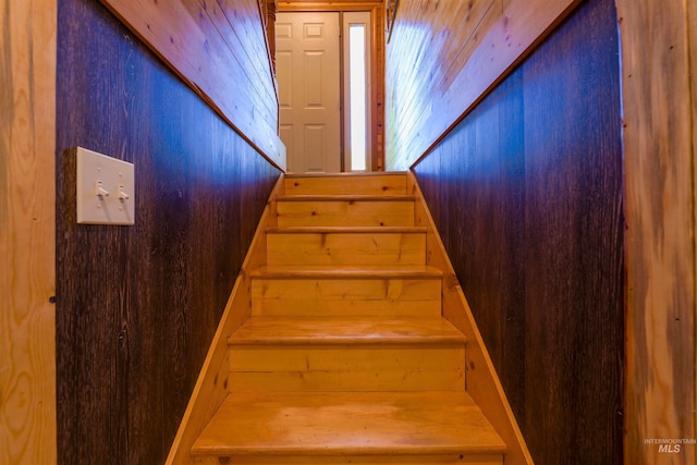 stairway featuring wooden walls