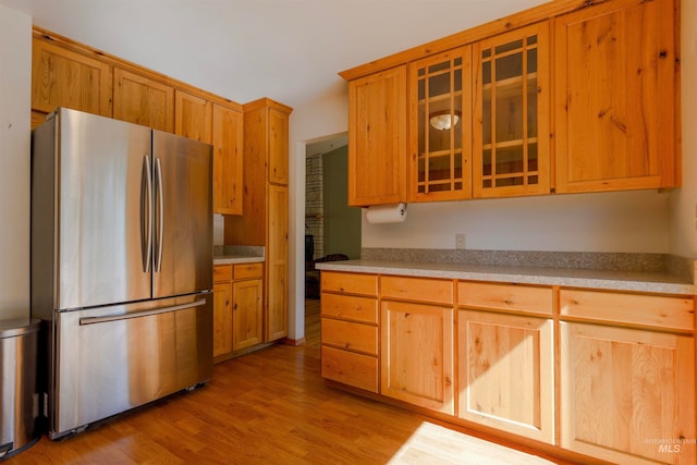kitchen with light countertops, light wood finished floors, glass insert cabinets, and freestanding refrigerator