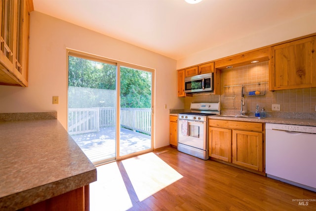kitchen with tasteful backsplash, light wood finished floors, brown cabinets, white appliances, and a sink