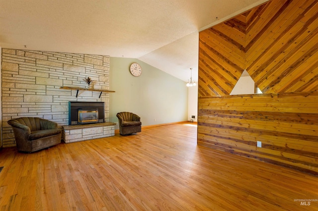 unfurnished living room featuring a stone fireplace, wood finished floors, and vaulted ceiling
