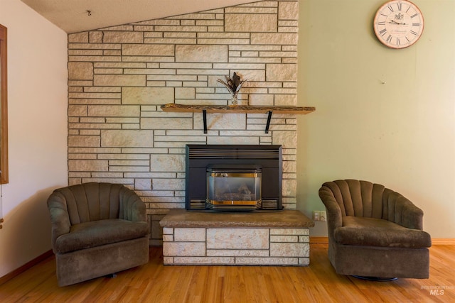 sitting room with a stone fireplace, wood finished floors, baseboards, and vaulted ceiling