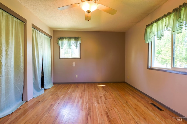 unfurnished bedroom featuring visible vents, multiple closets, light wood-style flooring, a textured ceiling, and baseboards