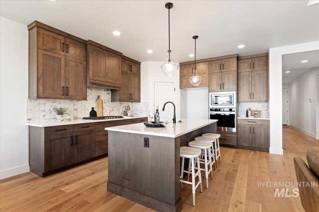 kitchen with backsplash, a kitchen island with sink, light hardwood / wood-style flooring, and stainless steel appliances