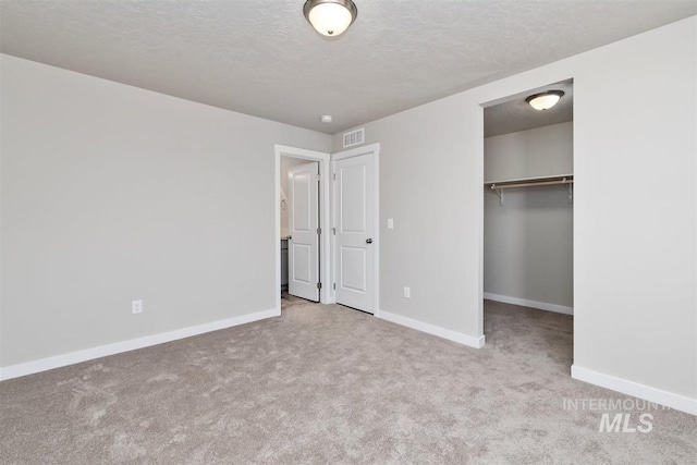 unfurnished bedroom featuring a walk in closet, a closet, light colored carpet, and a textured ceiling