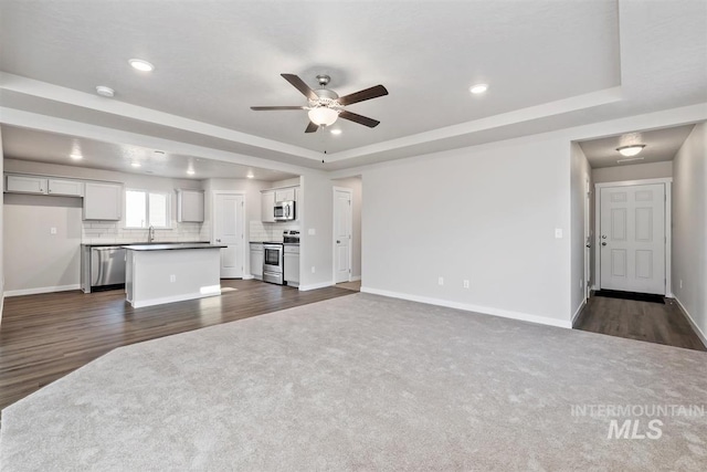 unfurnished living room with sink, ceiling fan, a raised ceiling, and dark wood-type flooring