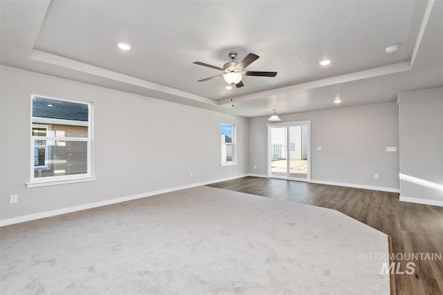 empty room featuring ceiling fan, a raised ceiling, and dark wood-type flooring