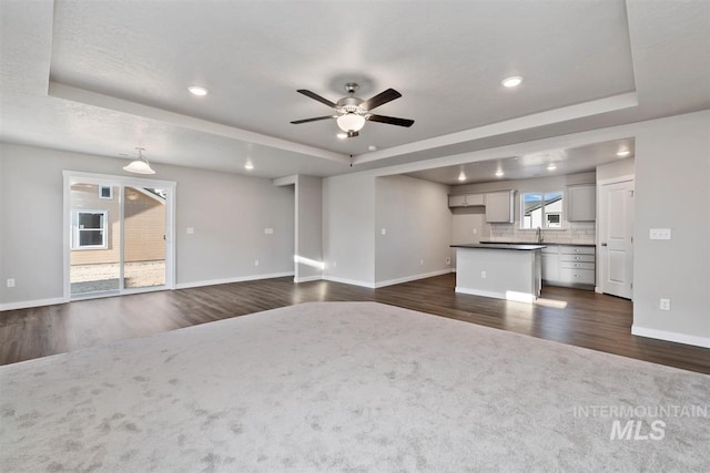 unfurnished living room with ceiling fan, a raised ceiling, and a wealth of natural light