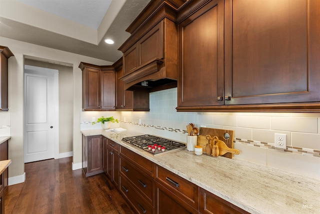 kitchen with tasteful backsplash, stainless steel gas cooktop, dark hardwood / wood-style flooring, custom range hood, and light stone counters