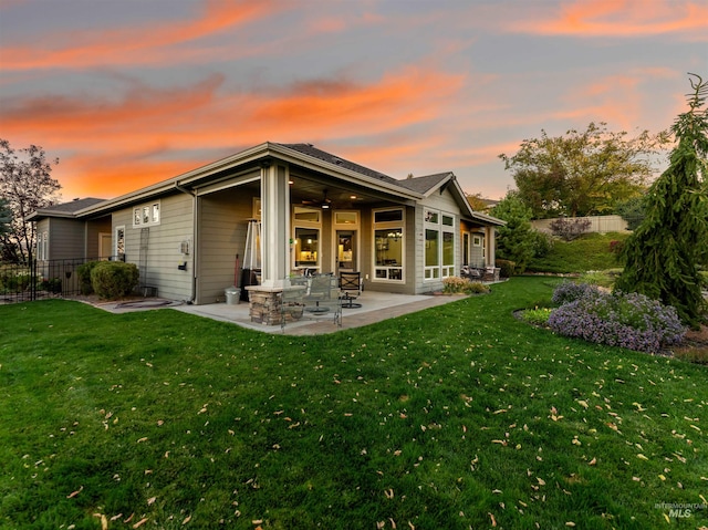 back house at dusk with a patio, a lawn, and ceiling fan