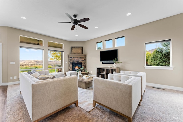 living room featuring ceiling fan, a stone fireplace, carpet flooring, and a wealth of natural light