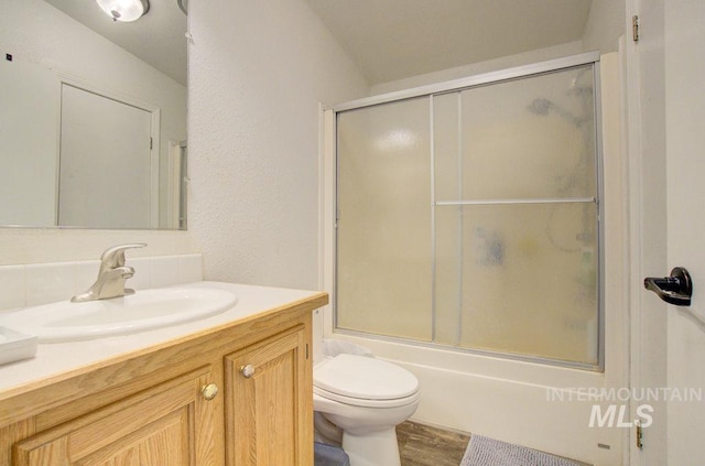 full bathroom with vanity, hardwood / wood-style flooring, bath / shower combo with glass door, and toilet