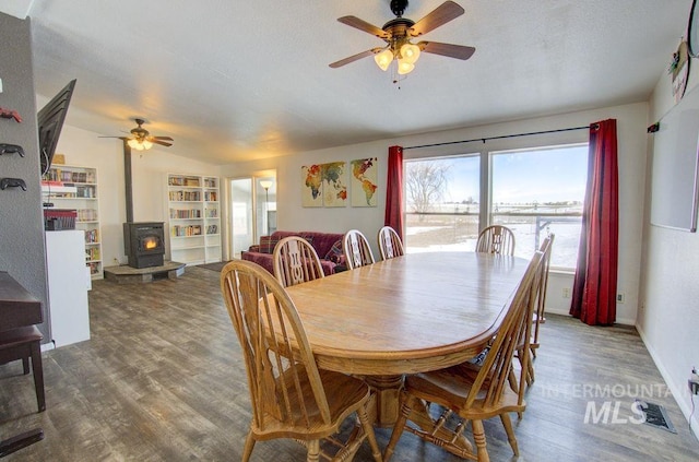 dining area featuring dark wood-type flooring, a wood stove, and ceiling fan