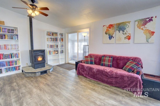 living room featuring vaulted ceiling, hardwood / wood-style floors, built in features, a wood stove, and ceiling fan