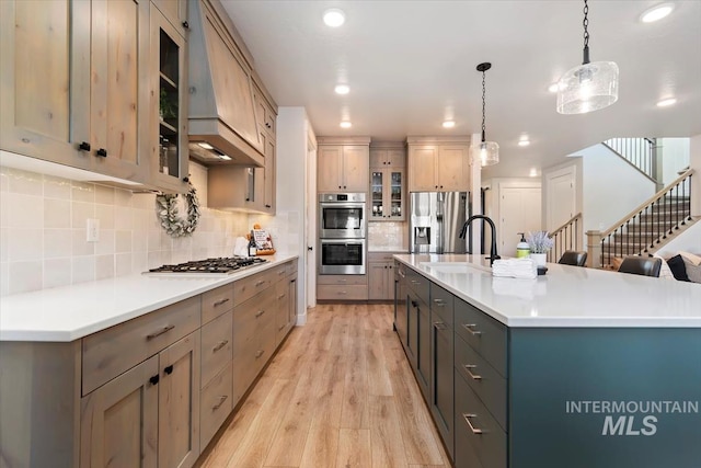 kitchen with stainless steel appliances, light wood finished floors, glass insert cabinets, backsplash, and decorative light fixtures