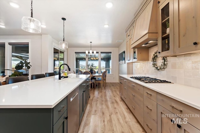 kitchen featuring a sink, stainless steel appliances, light wood-style floors, light countertops, and glass insert cabinets