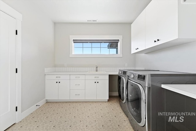 laundry area featuring independent washer and dryer, cabinet space, light flooring, and baseboards