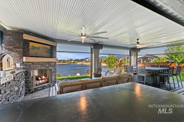 view of patio / terrace with a ceiling fan, a water view, and an outdoor living space with a fireplace