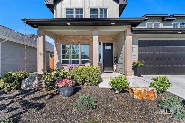 view of exterior entry with board and batten siding, brick siding, a porch, and driveway