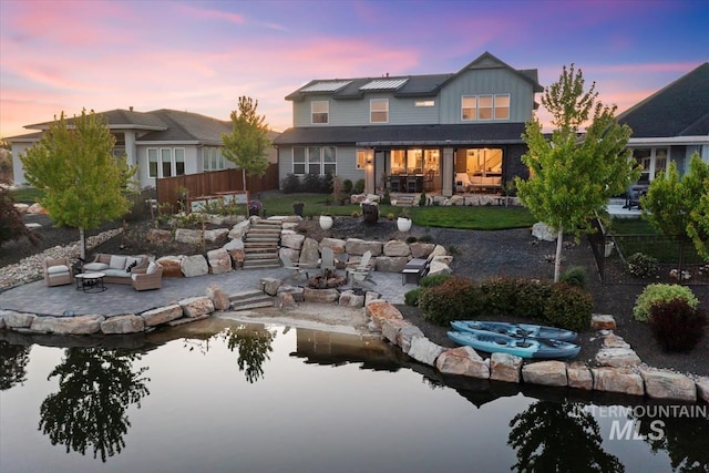 back of house at dusk featuring a patio area, board and batten siding, an outdoor hangout area, and a small pond