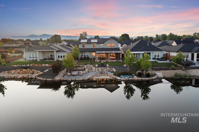 back of house at dusk with a residential view, a water view, and a patio area
