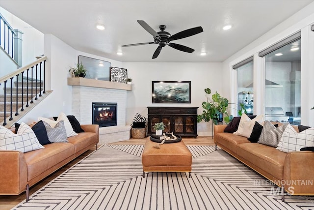 living room featuring a fireplace, wood finished floors, stairway, recessed lighting, and ceiling fan