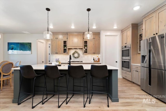 kitchen with appliances with stainless steel finishes, light countertops, backsplash, glass insert cabinets, and a kitchen breakfast bar