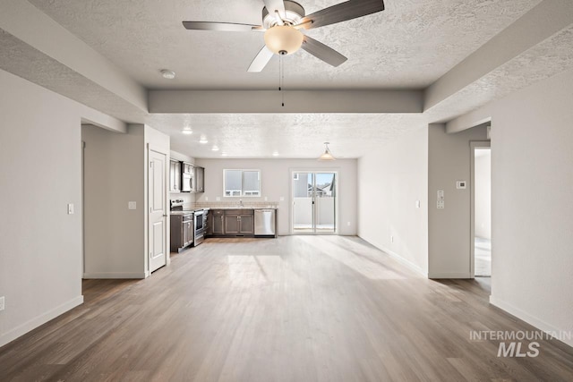 unfurnished living room featuring light wood-type flooring, a textured ceiling, and baseboards