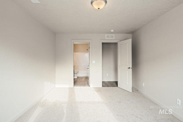 unfurnished bedroom featuring a textured ceiling, connected bathroom, carpet flooring, visible vents, and baseboards