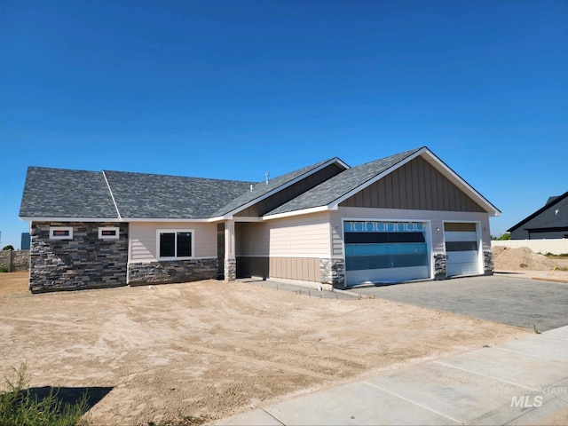 view of front of property featuring an attached garage, a shingled roof, stone siding, driveway, and board and batten siding