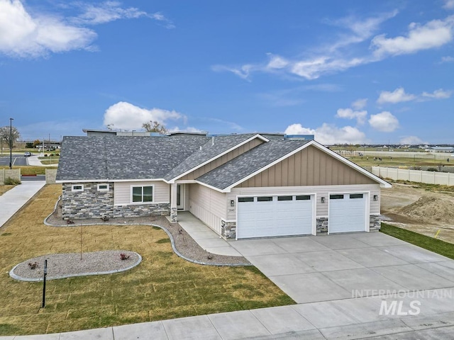 view of front of home with stone siding, an attached garage, a shingled roof, a front lawn, and driveway