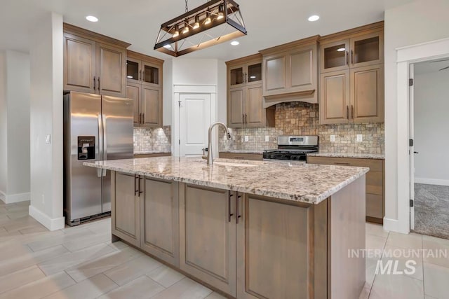 kitchen featuring glass insert cabinets, appliances with stainless steel finishes, a sink, and an island with sink