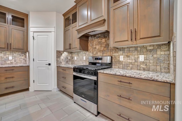 kitchen with glass insert cabinets, gas stove, light stone counters, and tasteful backsplash