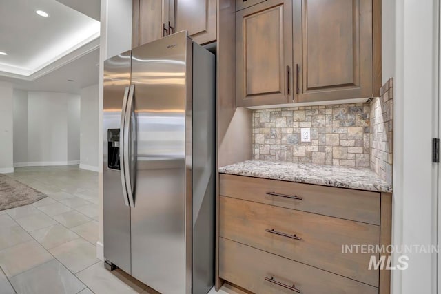 kitchen with light stone counters, recessed lighting, baseboards, backsplash, and stainless steel fridge with ice dispenser