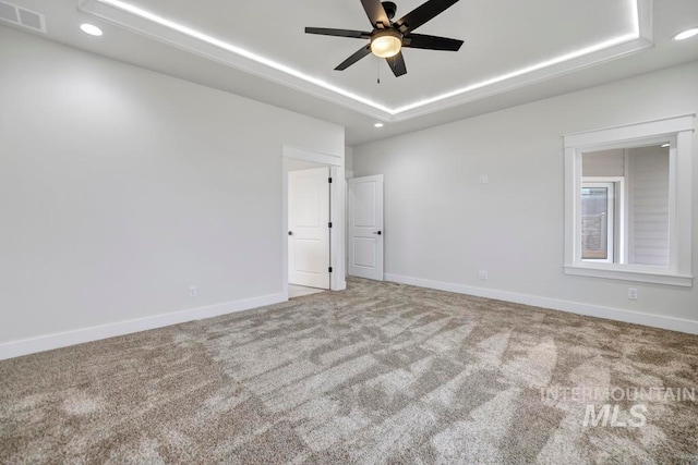 empty room featuring carpet floors, a tray ceiling, visible vents, and baseboards