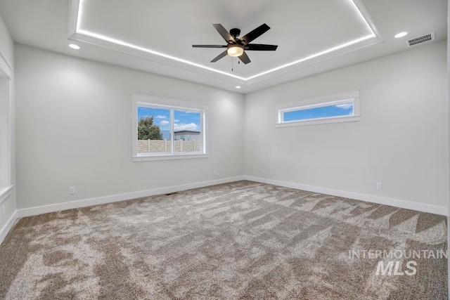 empty room featuring carpet, recessed lighting, a raised ceiling, visible vents, and baseboards