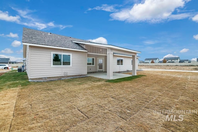 rear view of house with a yard, a shingled roof, board and batten siding, and a patio area