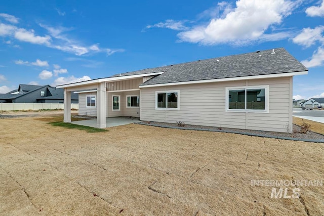 rear view of house featuring a shingled roof, a patio, fence, a yard, and board and batten siding