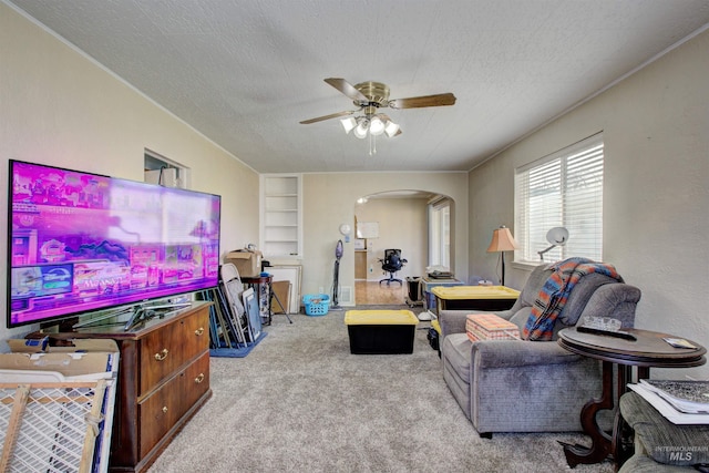 living area featuring ceiling fan, carpet, built in features, arched walkways, and a textured ceiling