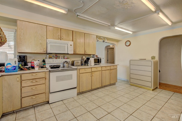 kitchen featuring light brown cabinetry, light countertops, light tile patterned floors, arched walkways, and white appliances