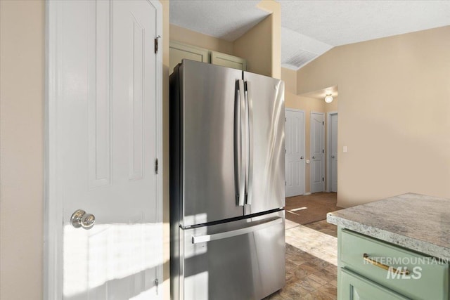 kitchen with stainless steel refrigerator, a textured ceiling, vaulted ceiling, and green cabinetry