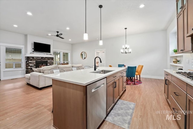 kitchen with sink, a center island with sink, light hardwood / wood-style flooring, stainless steel dishwasher, and a fireplace