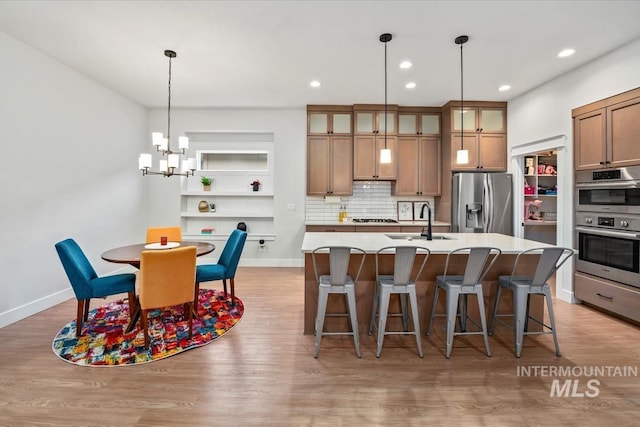 kitchen with sink, a breakfast bar, appliances with stainless steel finishes, an inviting chandelier, and a center island with sink