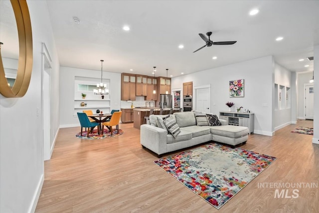 living room with ceiling fan with notable chandelier and light hardwood / wood-style flooring